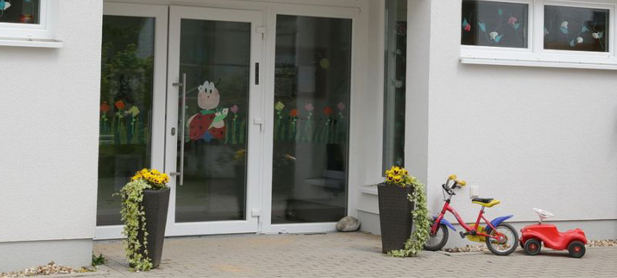 Der helle Eingangsbereich des evangelischen Kindergartens Loope mit einer Glastür und Pflanzentöpfen davor.