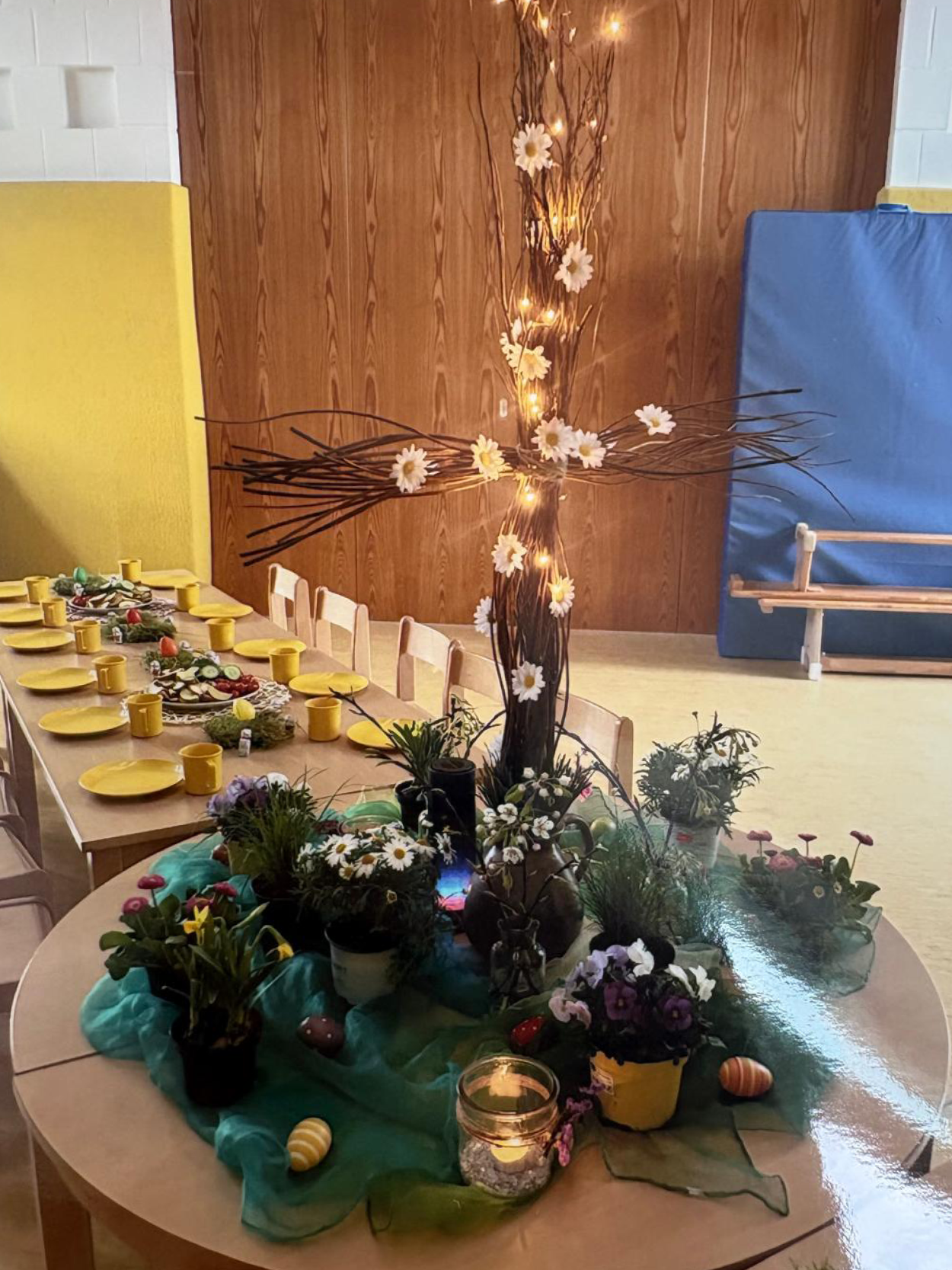 Ein lang und feierlich gedeckter Tisch im Gruppenraum, geschmückt mit Lichterketten und Tannenzweigen für ein gemeinsames Frühstück.