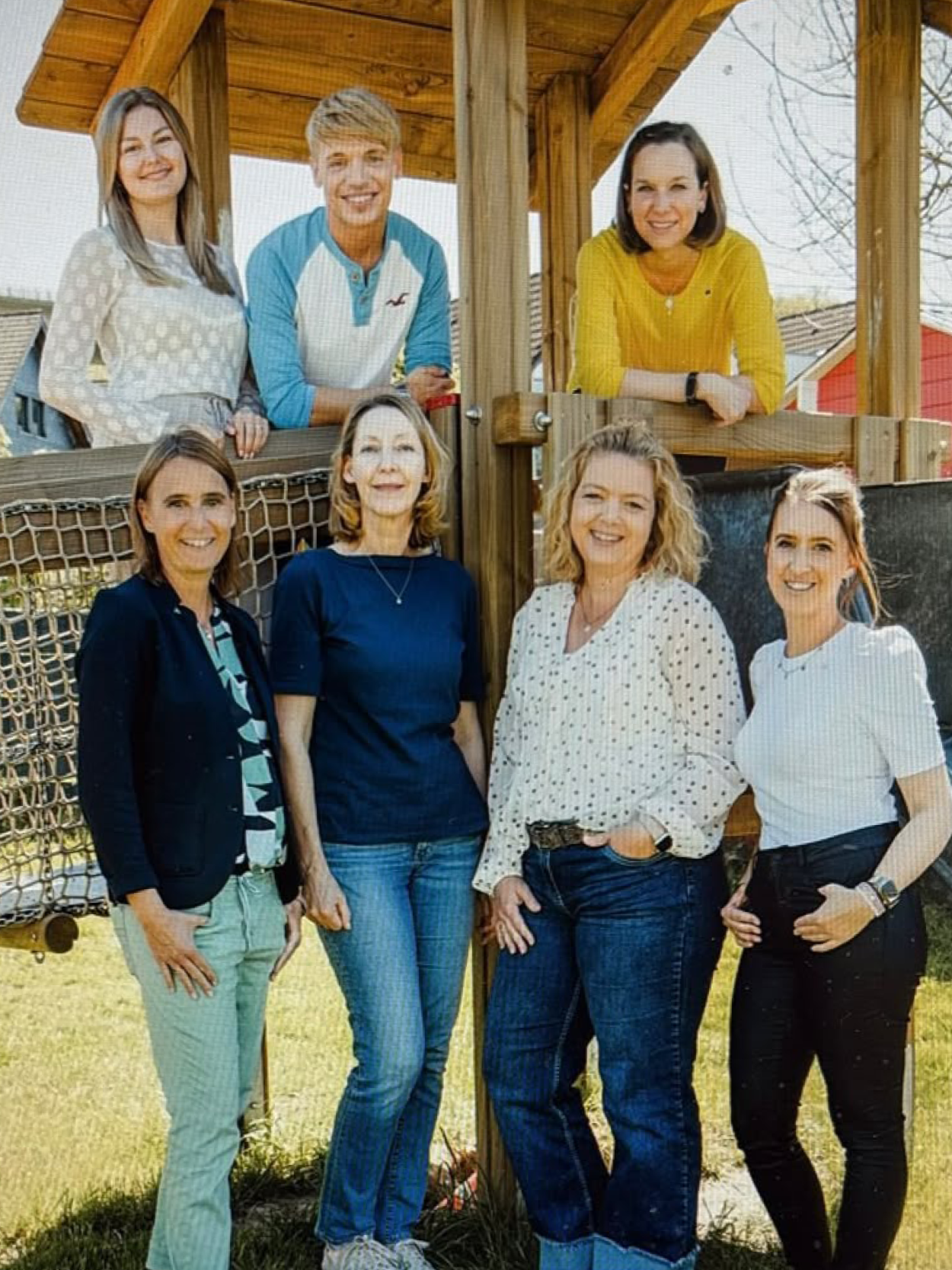 Gruppenfoto des engagierten pädagogischen Teams des evangelischen Kindergartens Loope vor einem Holzgerüst im Außengelände.